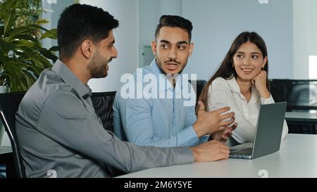 Multiethnic business team three office workers managers discus project online crypto currency brainstorm with laptop computer at workplace Stock Photo