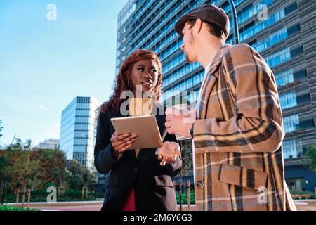 Colleagues using a digital tablet and talking about a new project while having a meeting outdoors. Stock Photo