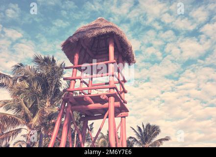 Wooden lifeguard tower on a Caribbean beach against the sky with coconut palm trees in background, color toning applied. Stock Photo