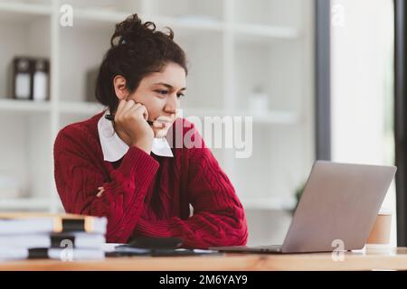 American Woman looking stressed while using laptop with financial document on table. Woman work from home Stock Photo