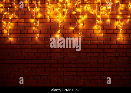 Yellow lights garlands hanging from red brick wall at evening, beautiful christmas house decoration with magic holiday atmosphere. Festive Christmas g Stock Photo