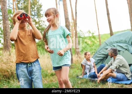 Boy looking through binoculars standing by happy sister while camping with family Stock Photo