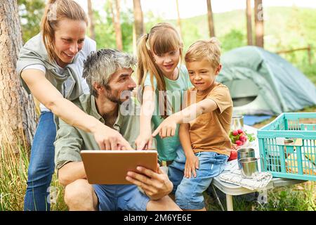 Family pointing at digital tablet held by man while camping in forest during vacation Stock Photo