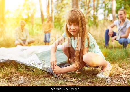 Girl setting up tent in summer while camping with parents and brother Stock Photo