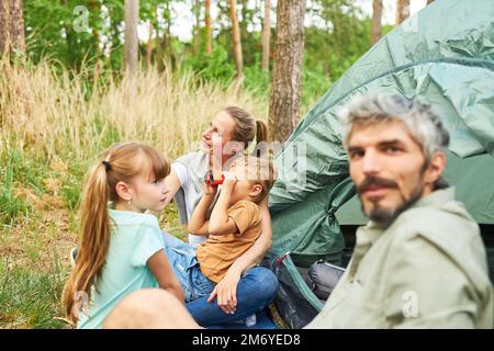 Boy looking through binoculars sitting by family at campsite during summer vacation Stock Photo