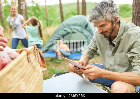 Man using digital tablet with family in background enjoying at campsite Stock Photo