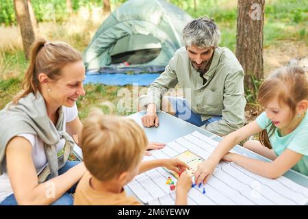Children playing ludo with mother and father during camping in forest on vacation Stock Photo
