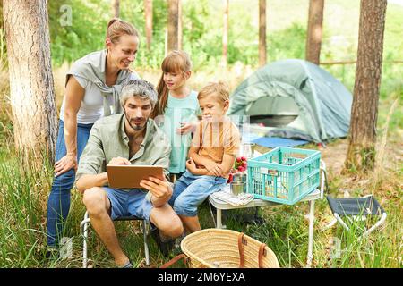 Man using digital tablet camping with family in forest during summer holiday Stock Photo