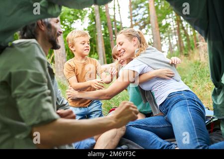 Happy mother embracing daughter and son while sitting in tent during forest Stock Photo
