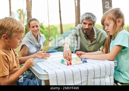 Man playing board game with children and sitting by woman at campsite during summer vacation Stock Photo