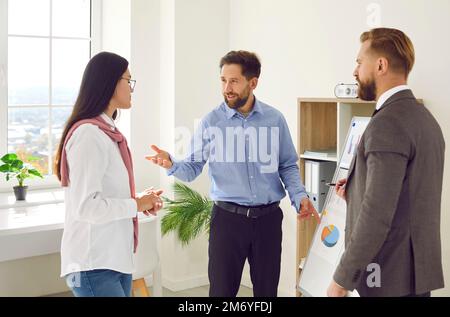 Colleagues near whiteboard talking and discussing ideas during brainstorming in office. Stock Photo