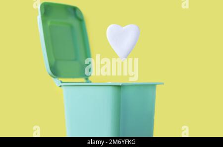 white ceramic heart shape falling in mini small green color trash garbage bin can.against valentines day holiday no celebration february 14th disappoi Stock Photo