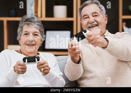 Video game, portrait and senior couple on sofa relaxing, bonding and gaming together in living room. Happy, fun and elderly man and woman gamers in Stock Photo