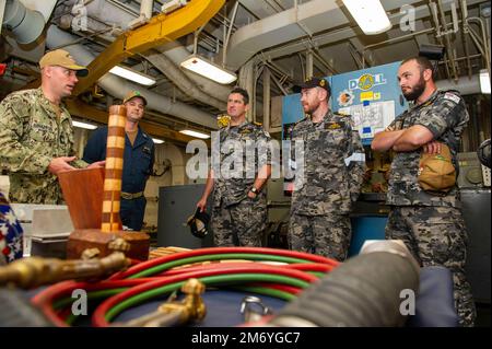 PERTH, Australia (April 19, 2022) U.S. Navy Cmdr. Brian Banazwski, the repair officer aboard the Emory S. Land-class submarine tender USS Frank Cable (AS 40), explains the repair capabilities of the ship to Royal Australian Navy sailors assigned to the RAN Collins-class submarine HMAS Farncomb (SSG 74) during a tour of the ship at HMAS Stirling naval base, April 19, 2022. Frank Cable is currently on patrol conducting expeditionary maintenance and logistics in support of national security in the U.S. 7th Fleet area of operations. Stock Photo