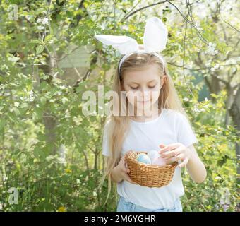 Cute little child wearing bunny ears on Easter day. Girl holding basket with painted eggs. Stock Photo