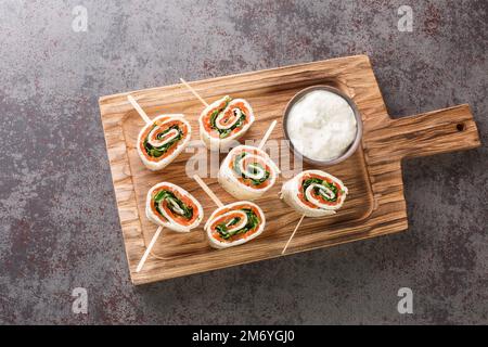 Rolls of thin pancakes with smoked salmon, cream cheese, arugula closeup on the board on the table. Horizontal top view from above Stock Photo