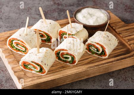 Rolls of thin pancakes with smoked salmon, cream cheese, arugula closeup on the board on the table. Horizontal Stock Photo