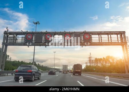 Dense stream of trucks and cars on a highway with speed signs of 110 km per hour in the morning at sunrise Stock Photo