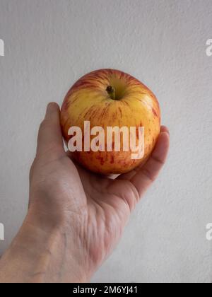 A woman's hand holding a ripe red apple against a white background. Ready-to-eat fruit Stock Photo