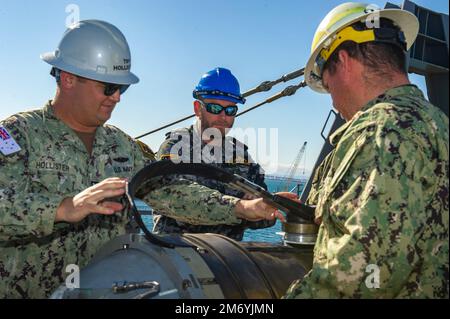 PERTH, Australia (April 20, 2022) – Torpedoman’s Mate 1st Class Robert Hollister (left), Torpedoman’s Mate 1st Class Cris Debeer, both assigned to the Emory S. Land-class submarine tender USS Frank Cable (AS 40), and Royal Australian Navy Chief Scott Schluter participate in a weapons handling training exercise with a Tomahawk training shape aboard the ship at HMAS Stirling Navy Base on Garden Island off the coast of Perth, Australia, April 20, 2022. Frank Cable is currently on patrol conducting expeditionary maintenance and logistics in support of national security in the U.S. 7th Fleet area o Stock Photo