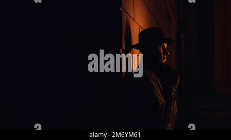 male mafia detective in a hat and raincoat at night in the style of film noir Stock Photo