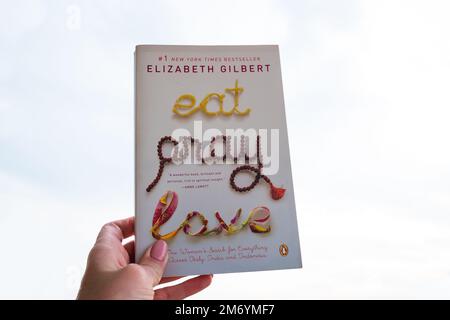 Milano, Italy - May 4, 2022: Hand holding New York Times bestseller by Elizabeth Gilbert 'Eat. Pray. Love'. Stock Photo
