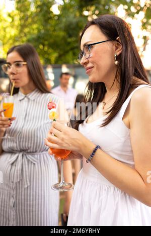 Happy female friends spending time together, young woman drinking Aperol spritz cocktail on outdoors wedding party. Happiness and celebration concpt Stock Photo