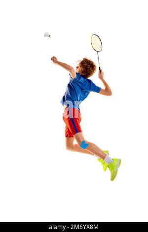 Portrait of teen boy in uniform playing badminton, serving shuttlecock with racket in a jump isolated over white background Stock Photo