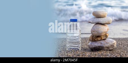 pebbles in pyramid one over another and bottle with drinking water on big rock beach sea waves in background.pure water.bottle and stones surrounded b Stock Photo