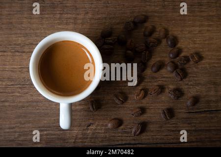 White cup of espresso with coffee beans on wooden table Stock Photo
