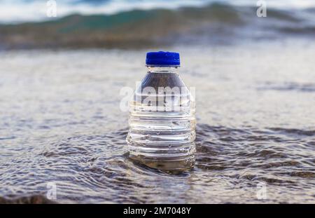 pebbles in pyramid one over another and bottle with drinking water on big rock beach sea waves in background.pure water.bottle and stones surrounded b Stock Photo