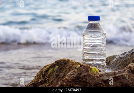 pebbles in pyramid one over another and bottle with drinking water on big rock beach sea waves in background.pure water.bottle and stones surrounded b Stock Photo