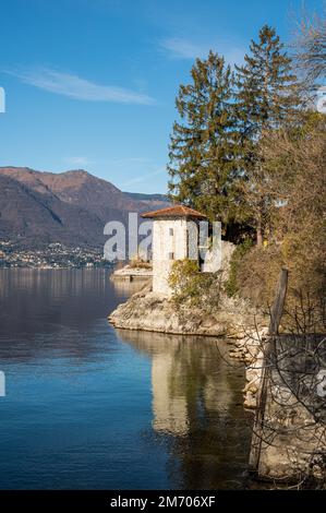 Castelveccana, Italy- 12-27-2022: Old ruined furnaces with chimneys with red bricks reflecting on the water of Lake Maggiore in the Parco delle Fornac Stock Photo