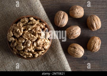 Bowl full of peeled walnuts and whole walnuts on a wooden background Stock Photo