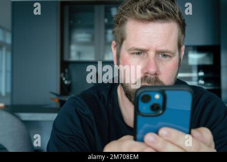Close up of young Caucasian man in glasses hold look at cellphone screen browse surf wireless internet. Millennial male use modern smartphone, texting Stock Photo