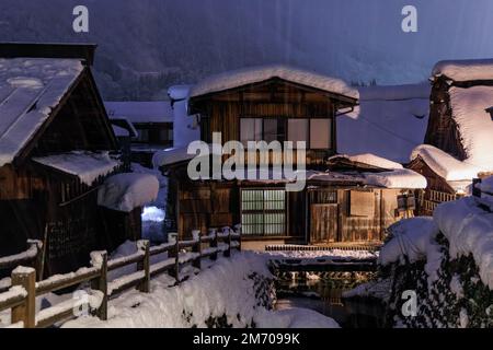 Heavy snow falls on traditional wooden homes in Japanese village at night Stock Photo