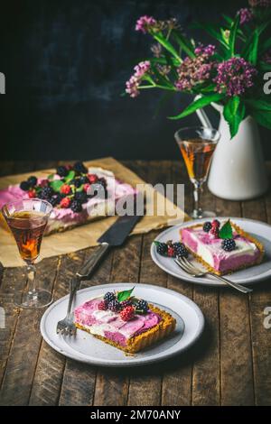 Cheesecake and berries on parchment with slices on serving plates and glasses of sherry Stock Photo