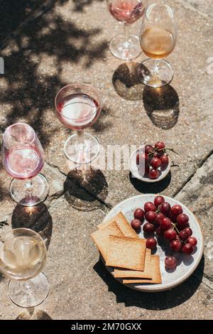 Glasses of rose and white wine with grapes and crackers shot in hard light on tiles Stock Photo