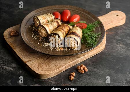 Grilled eggplant rolls stuffed with walnuts with tomatoes and fresh green dill. The plate is on the cutting board. Stock Photo