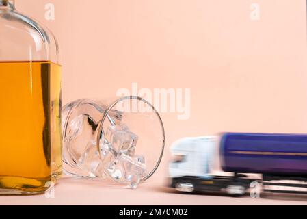 Whiskey bottle and glass lying with ice cubes, a toy tanker truck at high speed goes towards the glass to crash irretrievably. Stock Photo