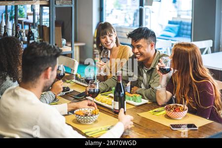 Young people dining and having fun drinking red wine together at restaurant, happy friends eating asian food,  Millenials life style concept, muted wa Stock Photo