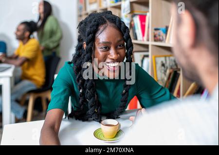 Young woman of African origins flirting with an unrecognizable man, people having breakfast in a bistro cafe, valentine’s day concept and dating coupl Stock Photo