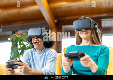 Two young women play virtual reality videogames, people using headsets and smart phones such as shrinking entertainment technology, virtual reality co Stock Photo