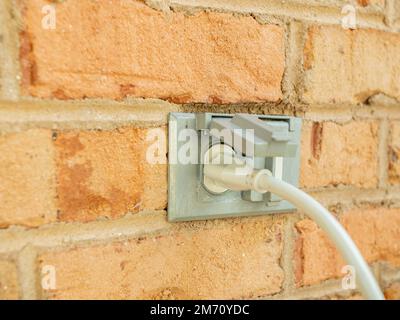 Power cord plugged into outdoor electrical wall socket. Dual covered electricity power outlets on brick wall. White extension cord plug. Stock Photo