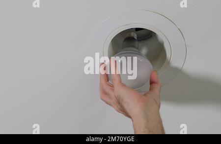 Electrician installing new light bulb in recessed ceiling light fixture. Man replacing burned out incandescent light bulb. Stock Photo