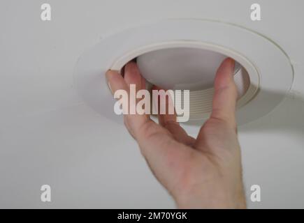 Electrician installing new light bulb in recessed ceiling light fixture. Man replacing burned out incandescent light bulb. Stock Photo