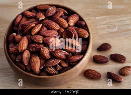 Bowl of roasted and salted whole almonds in wood bowl on wooden table. Stock Photo