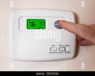 Closeup of a man's hand setting the room temperature on a programmable home thermostat. Stock Photo