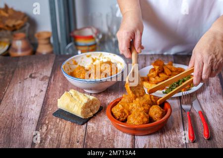Woman in white apron serving meatballs with a wooden tong in a clay pot Stock Photo