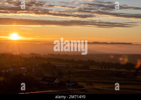 sunrise with sun shining into the camera above Dürrenmettstetten village in germany swabia with hazy landscape Stock Photo